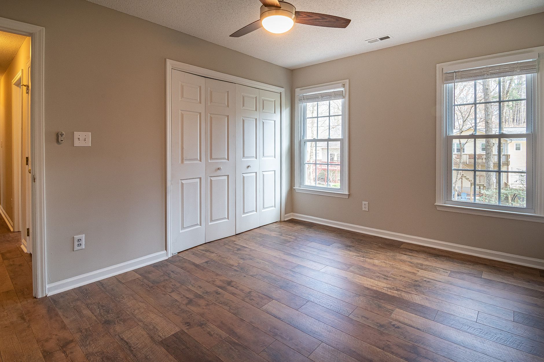 Spacious empty room with hardwood floors, ceiling fan, and natural light from windows
