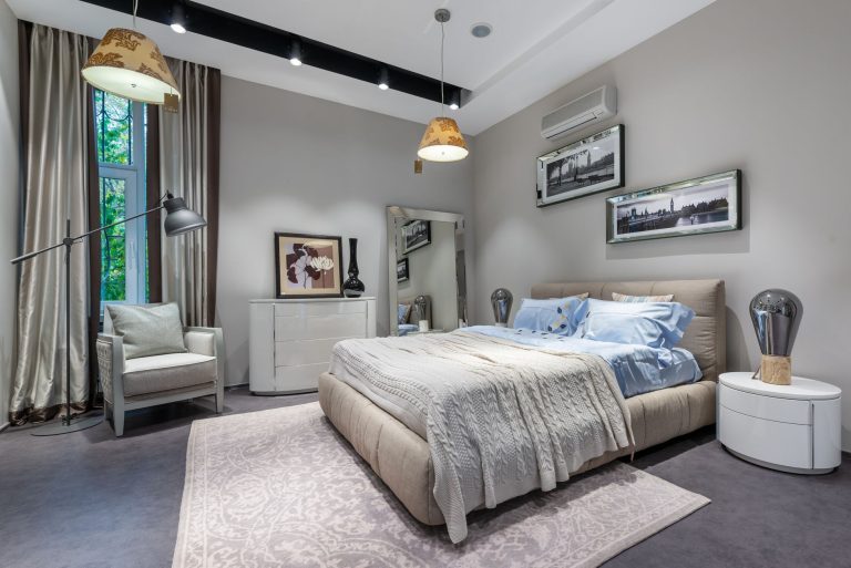 Grey fitted carpet in an Oregon bedroom with an upholstered bed, a pale rug and tall curtained windows