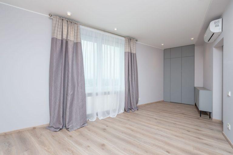 Light wood-look luxury vinyl plank flooring in an empty Oregon room with full-height curtains and pale grey walls