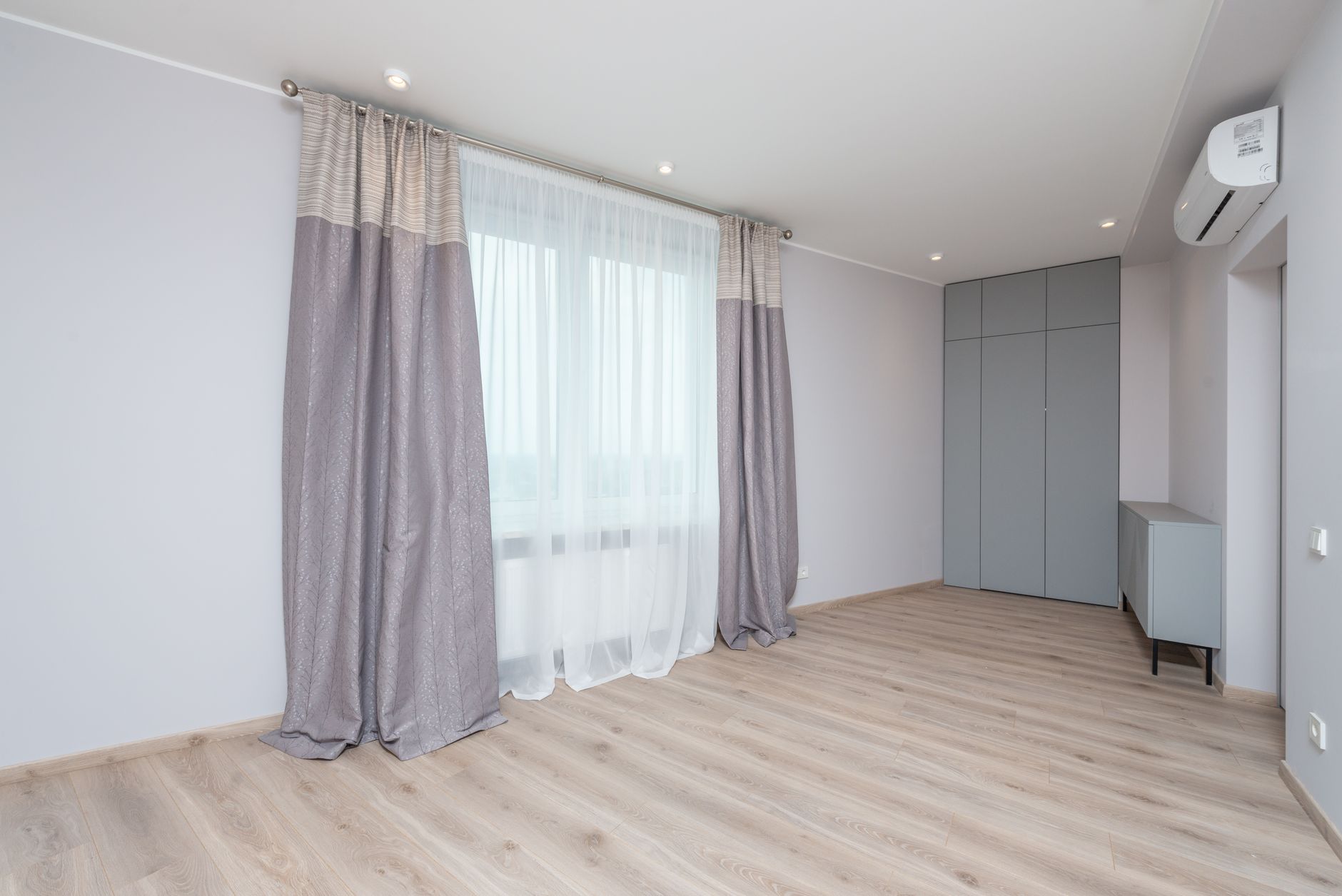 Light wood-look luxury vinyl plank flooring in an empty Oregon room with full-height curtains and pale grey walls