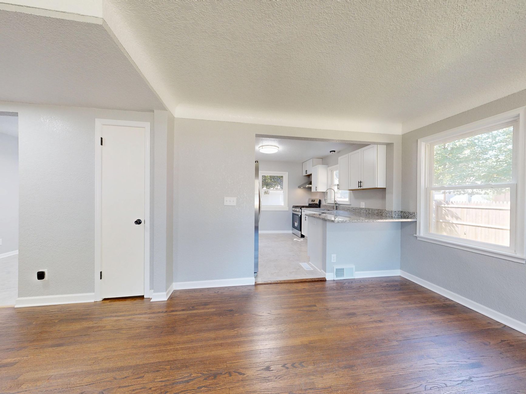 Refinished dark hardwood flooring running from an empty Oregon room through to the kitchen beyond