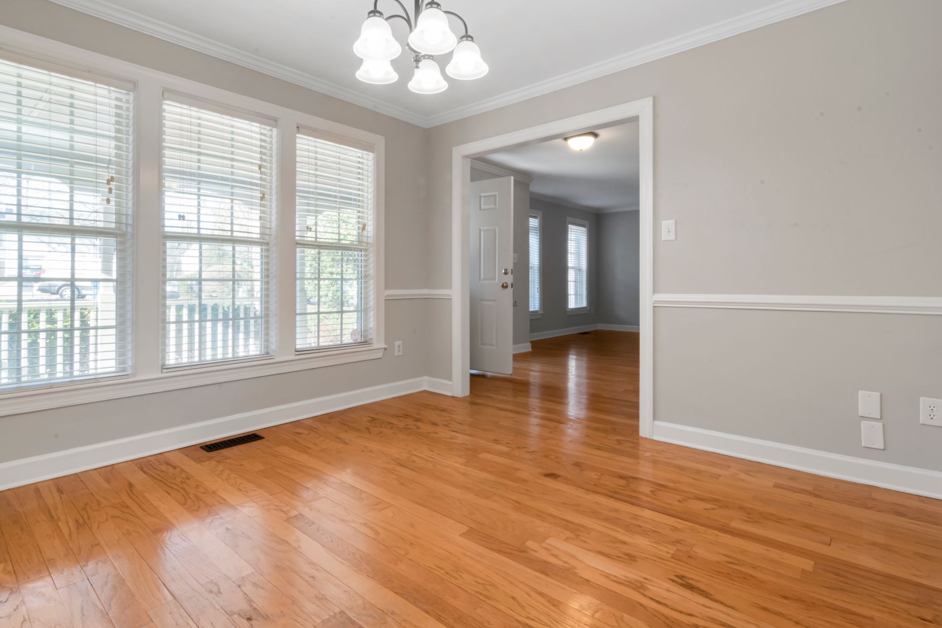 Warm oak hardwood flooring in an empty Oregon living room with tall shuttered windows and a doorway through to a second room