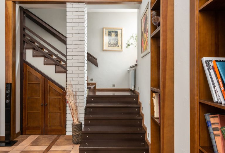 Dark wooden stair treads and risers in an Oregon home, running up past a painted brick pier and built-in bookshelves