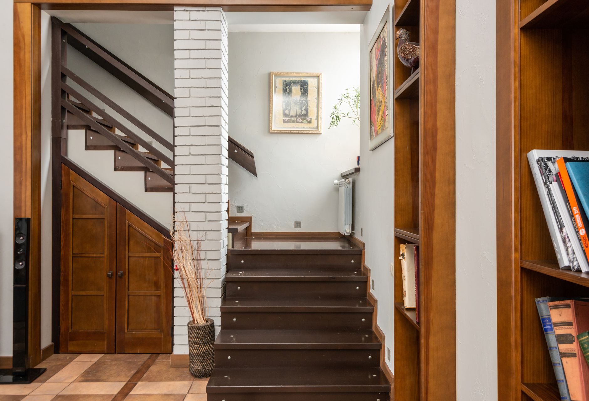Dark wooden stair treads and risers in an Oregon home, running up past a painted brick pier and built-in bookshelves