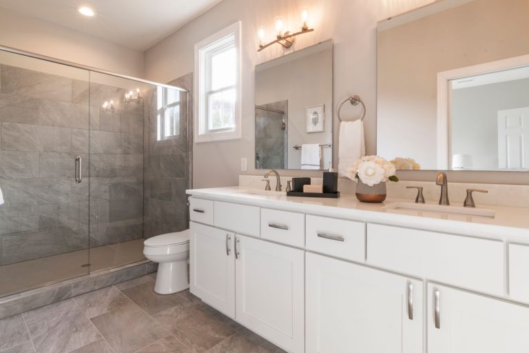 Grey large-format tile flooring in an Oregon bathroom with a white double vanity and a glass shower enclosure