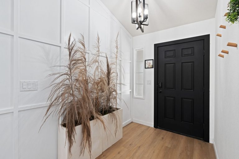 Light wood-look flooring in the entry of an Oregon home, a black front door with side lights and a planter of dried grasses